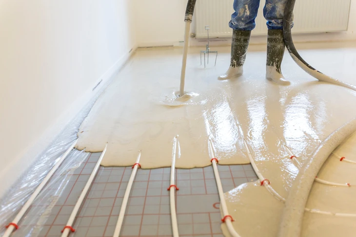 Technicien en combinaison blanche de protection intégrale avec masque à ventilation assistée, manipulant un flexible d'injection dans une pièce en rénovation