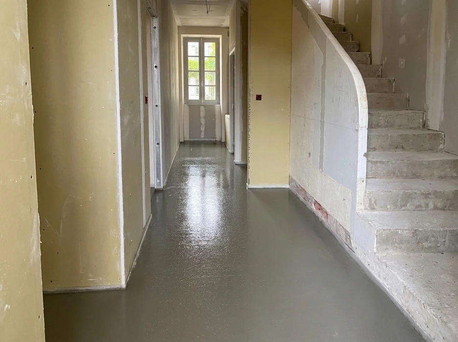 Couloir en rénovation avec sol en béton ciré gris lissé et brillant fraîchement appliqué
