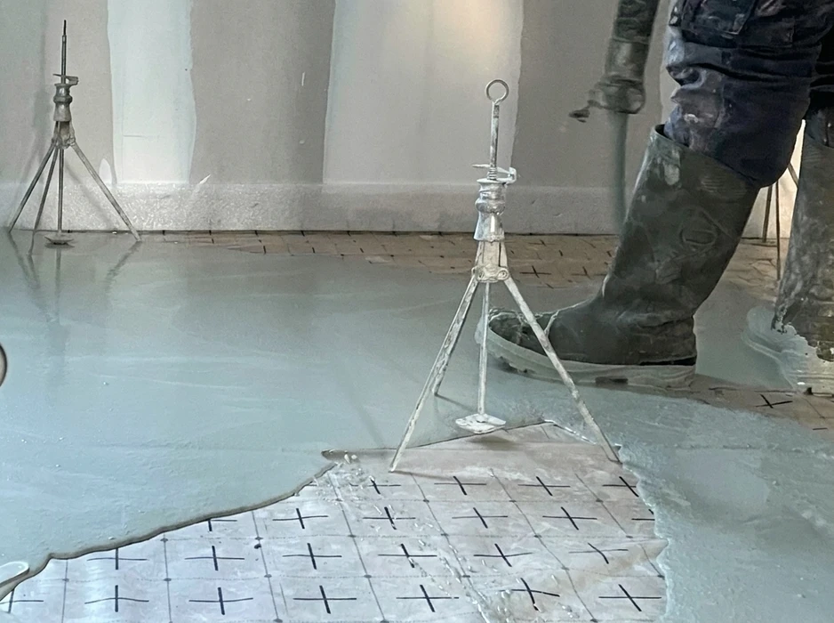 Ouvrier en bottes de caoutchouc debout sur une chape liquide fraîche en cours de coulage