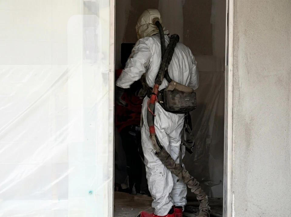 Ouvrier en combinaison de protection blanche applique de l'isolant thermique par projection dans les combles d'un bâtiment