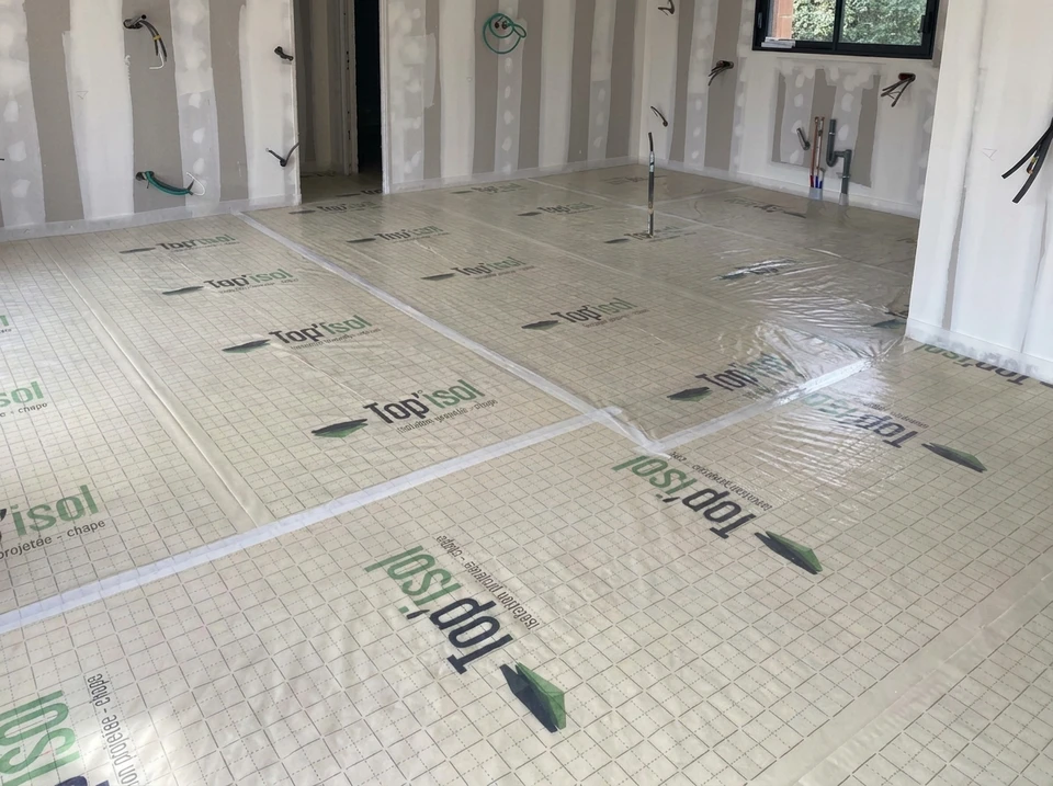 Technicien en combinaison blanche de protection intégrale avec masque à ventilation assistée, manipulant un flexible d'injection dans une pièce en rénovation