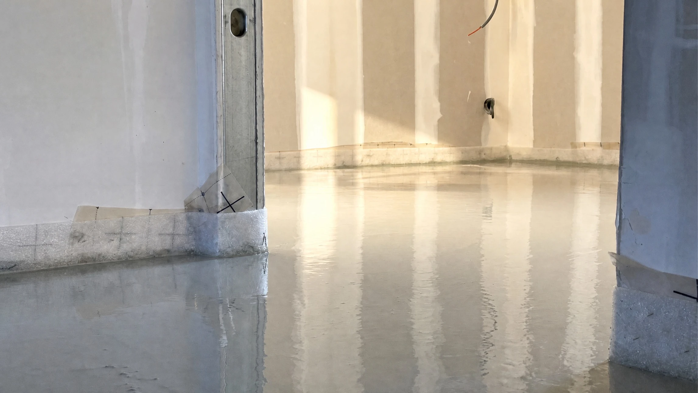Ouvrier en bâtiment agenouillé appliquant du mortier ou béton au sol intérieur avec règle de maçon